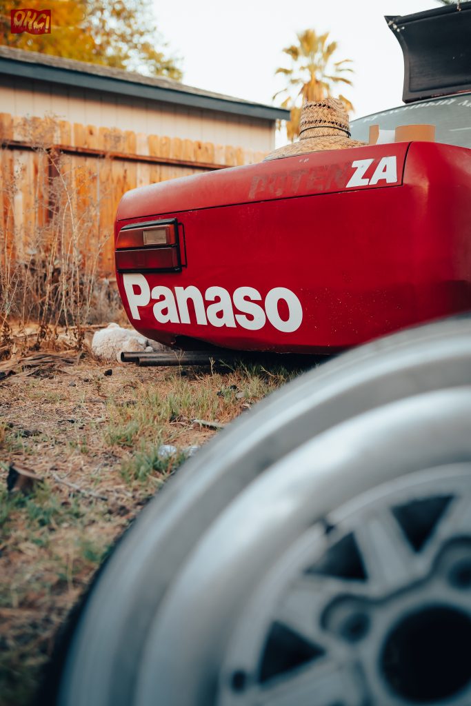 Close-up of a red vintage car with Panasonic partially visible, featuring text POTENZA and a straw hat on the rear.