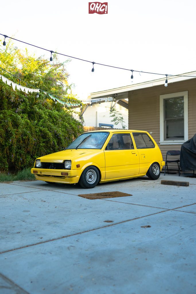 Retro yellow car parked in a cozy backyard under string lights; OHG! text in Japanese on a sign above.