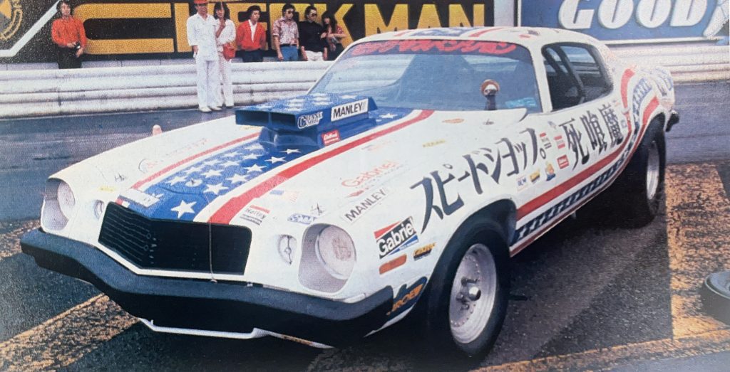 Vintage drag racing car with American flag design and Japanese text in front of spectators at the Circuit Showdown event.