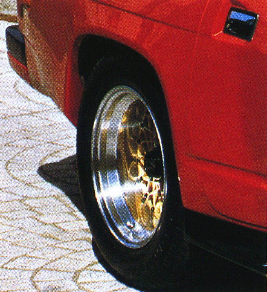 Close-up of a classic red car's wheel with golden mesh rims and low-profile tires on a paved surface.