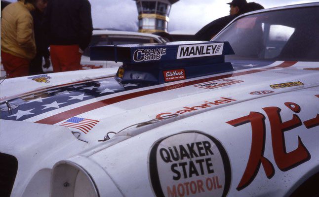 Race car with American flag design, featuring Quaker State Motor Oil and Gabriel stickers, and a tower in the background.