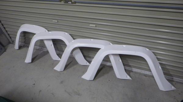 White automotive fender flares lined up against a closed garage door. Ideal for vehicle body modifications and protection.