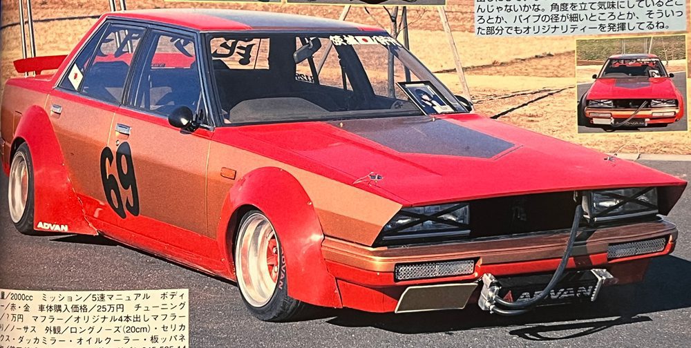 Vintage Japanese race car with number 69, featuring wide fenders, sponsors, and custom modifications parked on a racetrack.