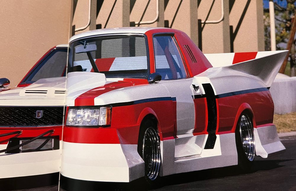 Highly-modified, red and white custom truck with aerodynamic body kits and large rear spoiler parked next to a similar vehicle.