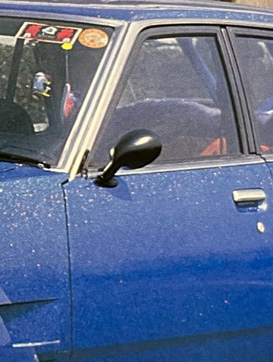 Vintage blue car with Japanese stickers on windshield, showcasing classic design and detailed exterior, captured in daylight.