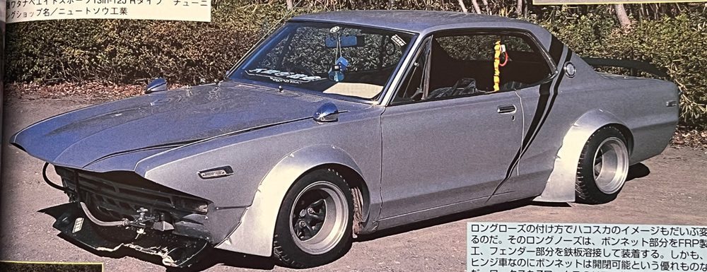Vintage modified gray Nissan Skyline GT-R with custom fenders and hood, displayed on a street with Japanese text descriptions.
