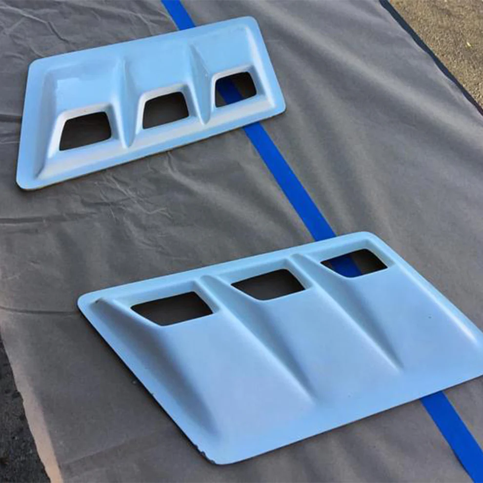 Two blue automotive body panels with vent openings on a gray surface, separated by a blue line.