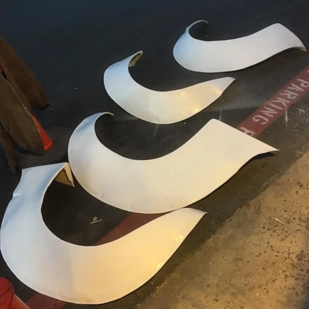 Moonlight Runners RX-3 Savanna fiberglass works over fender car fender flares laid out on asphalt next to a cone and a No Parking zone painted in red.