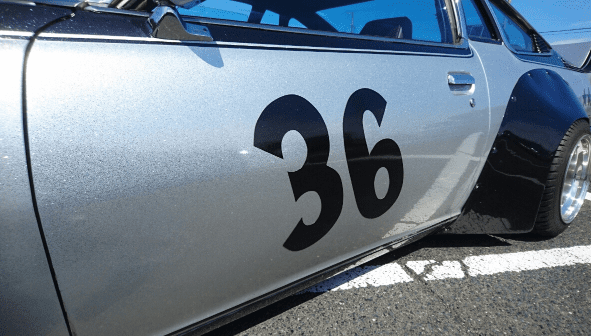 Silver race car with black number 36 on the door, showcased in a parking lot under clear blue skies.