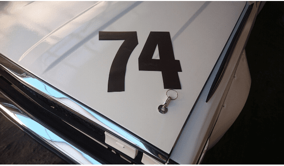 Alt text: Close-up of a car hood with the number 74 and a keychain lying on it