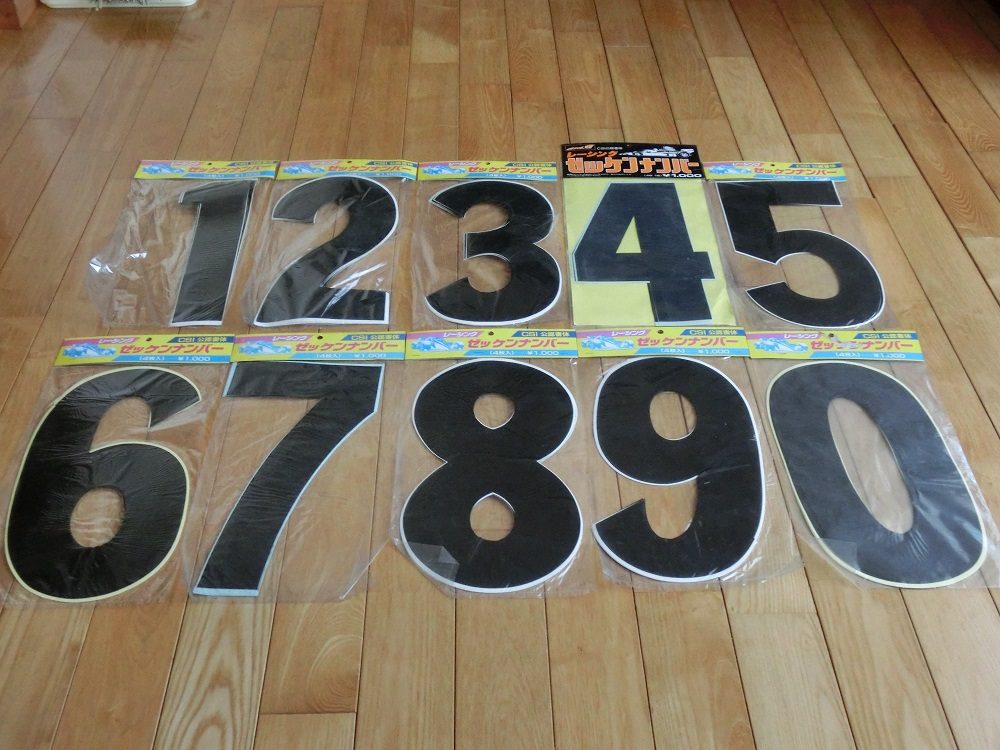 Large black adhesive numbers (0-9) on wooden floor, packaged in plastic with colorful Japanese labels, ideal for decorations.