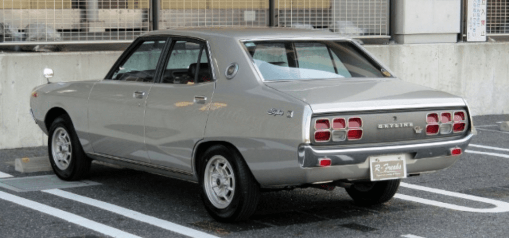 Vintage gray Nissan Skyline parked in a lot, showcasing its classic design and distinctive rear lights.