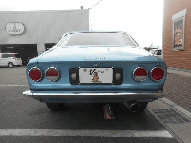 Rear view of a classic blue vintage car parked outside a garage with Vintage signage.
