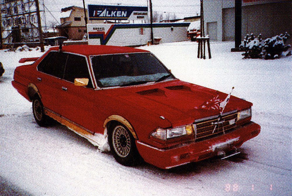 Modified red sedan with a spoiler and front flags parked on a snowy street.