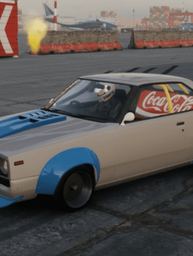 Modified vintage car with Coca-Cola banner on the side at an industrial area, painted in blue and white.