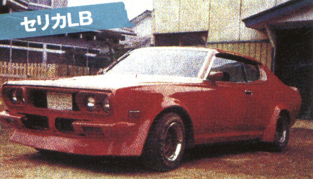 Red classic sports car parked by a wooden fence, featuring angular design and retro styling.