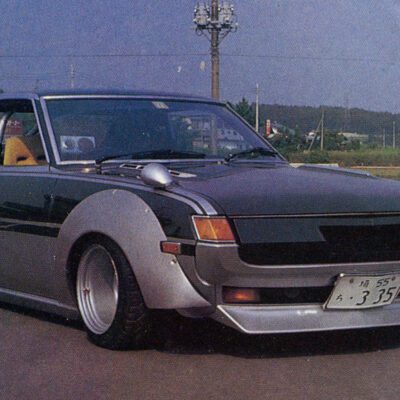 Vintage modified car with wide fenders and sleek design parked on a road with landscape in background.