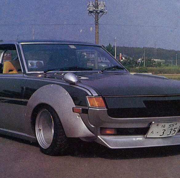 Vintage modified car with wide fenders and sleek design parked on a road with landscape in background.