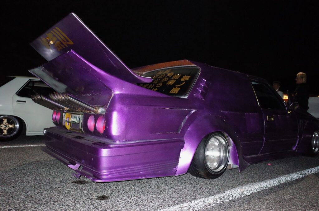 Purple customized kaido racer with large rear spoiler and unique design at night.