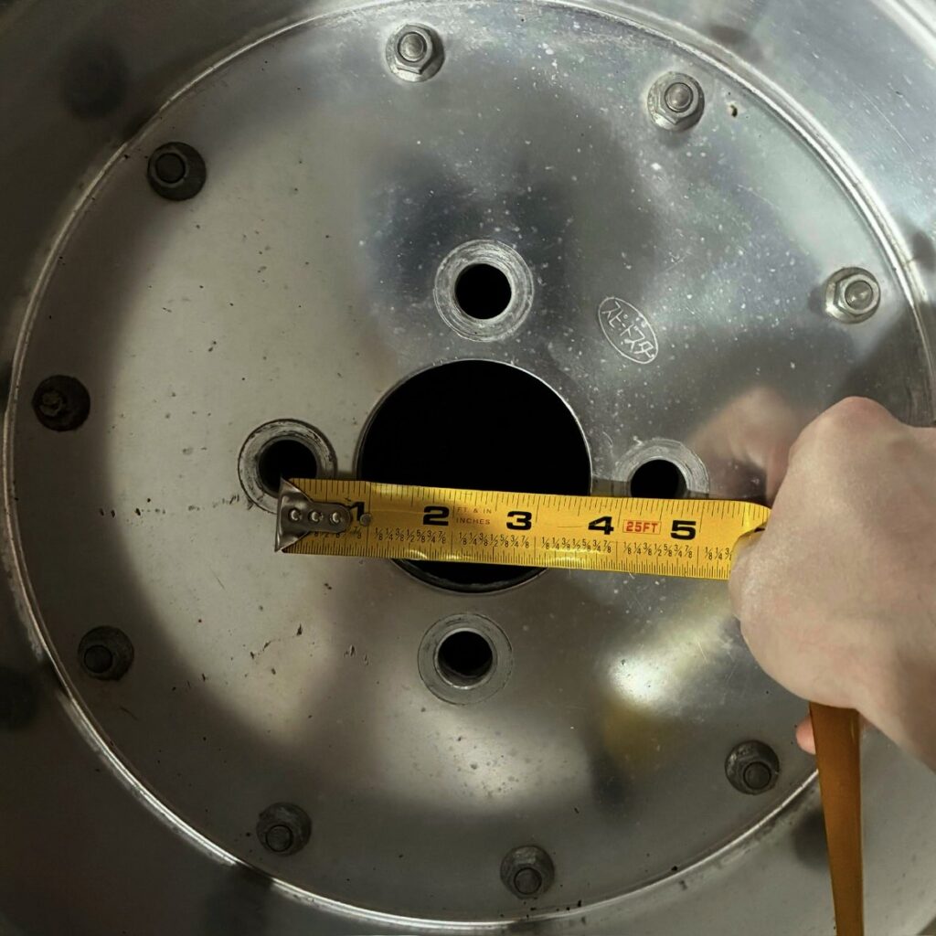 Measuring wheel rim diameter with a yellow tape measure held by a hand.