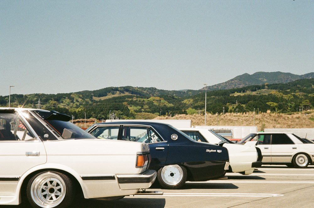 Vintage cars parked against scenic mountain backdrop, showcasing classic automotive design.