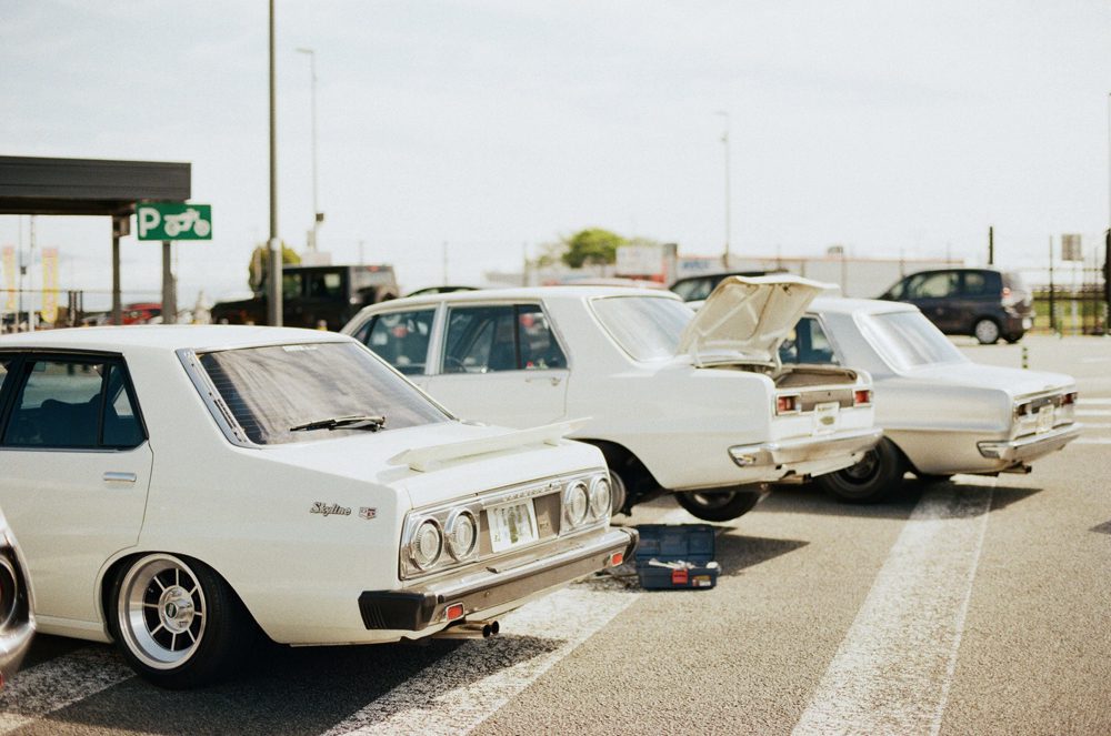 Classic white cars parked outdoors with opened trunks under a sunny sky.