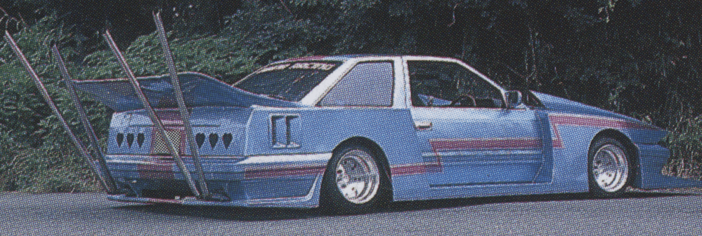 Blue custom car with red stripes, large rear wing, and extended exhaust pipes parked on a road.
