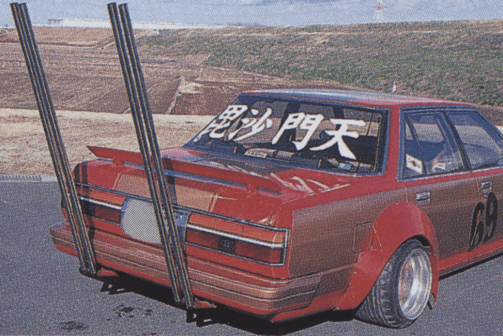Custom red car with tall exhaust pipes and Japanese text on rear windshield in bozosoku style.