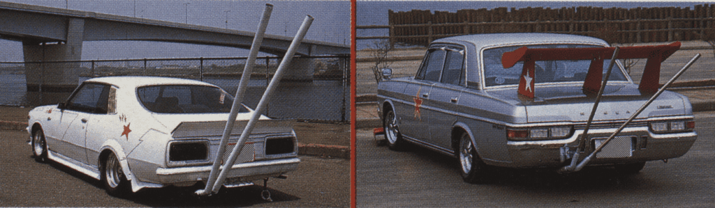 Modified classic cars with custom tall exhausts and large rear wings, parked near a bridge.
