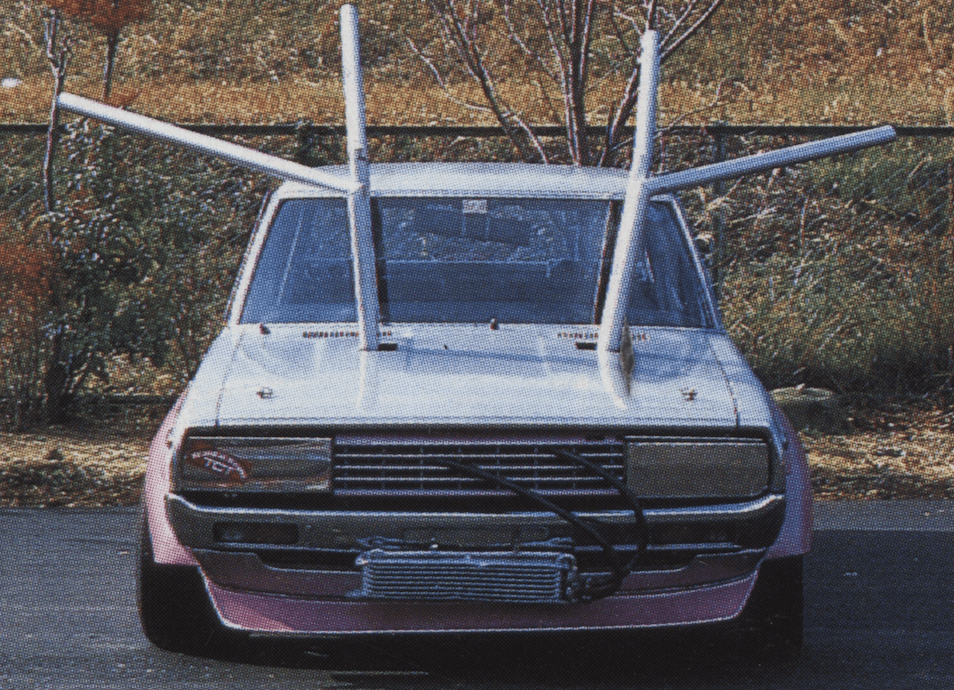 Quirky modified car with large metal rods extending from the hood, parked outdoors.