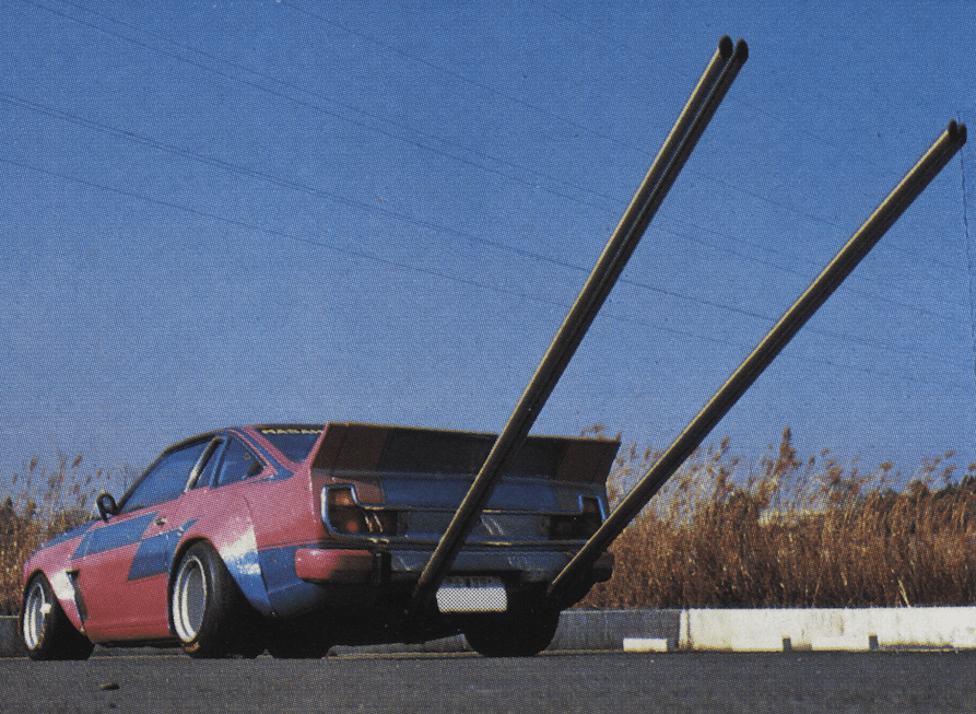 Sporty car with exaggerated long exhaust pipes and bold design, parked on a road under a clear blue sky.