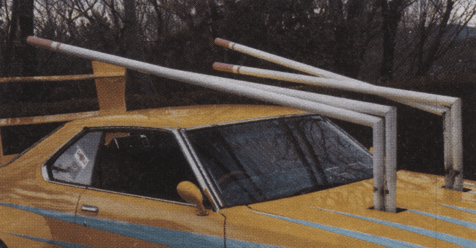 Yellow car with unique roof pipes resembling pencils, surrounded by trees. Creative and unconventional design.