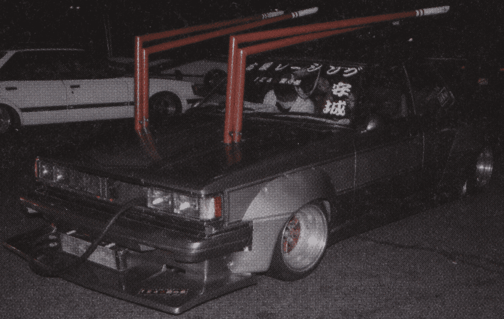 Vintage car with large red exhaust pipes, decorated windshield, nighttime scene, and retro styling.