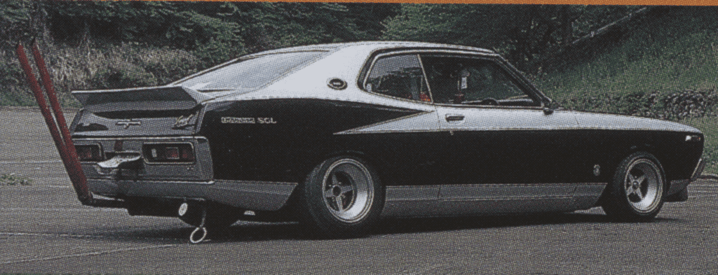 Vintage custom car with exaggerated exhaust pipes in a scenic setting.
